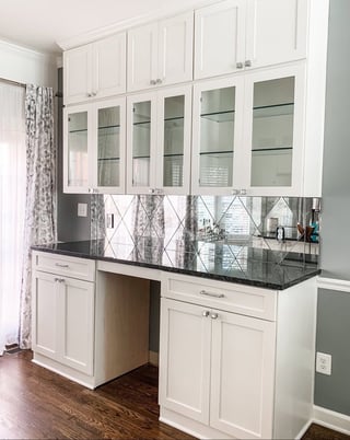 Modern white kitchen cabinetry with black granite countertops, glass-front upper cabinets, and geometric patterned backsplash