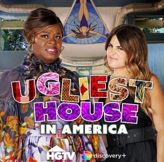 Two women posing in front of Ugliest House in America logo and blue stained glass window for HGTV show