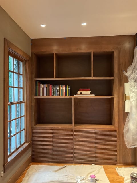 Wooden walk-in closet with built-in shelving, glass-paned window, recessed lighting, and lower cabinet storage with horizontal slats