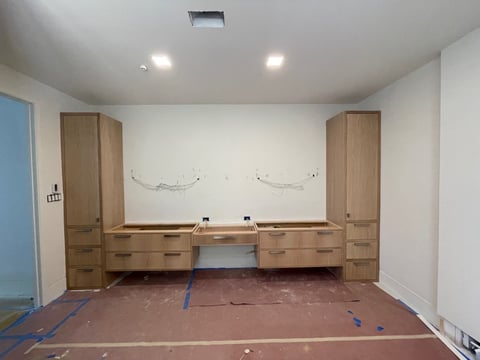 Modern bathroom under construction with wooden vanities, white walls, recessed lighting, and protective floor covering