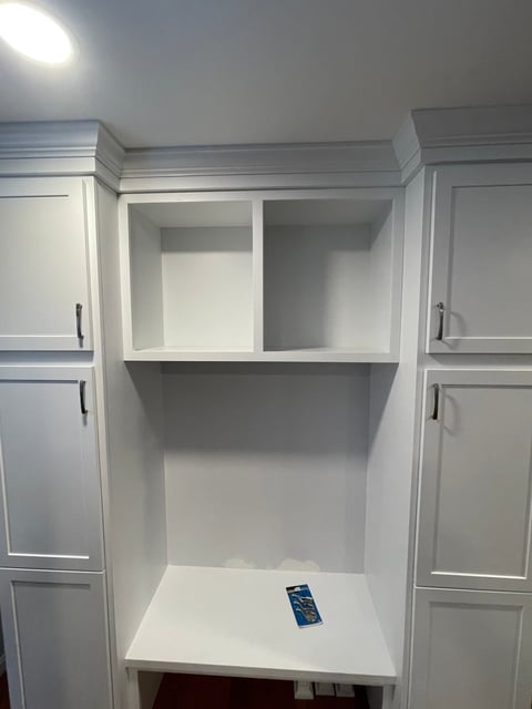 White kitchen cabinet with open shelving showing two compartments above a lower shelf, with dark handle hardware visible