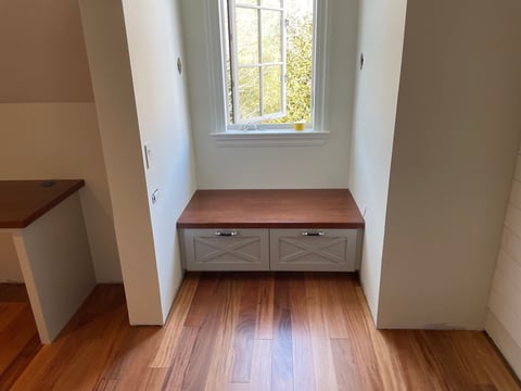 Hallway with wooden bench and storage, natural light from window, white walls and wooden flooring