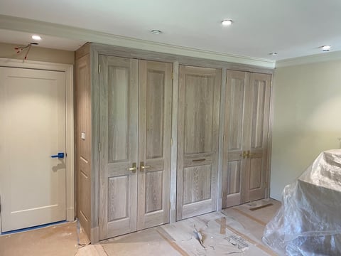 Bedroom interior with large wooden wardrobe closet doors, beige walls, recessed ceiling lights, and white door on left