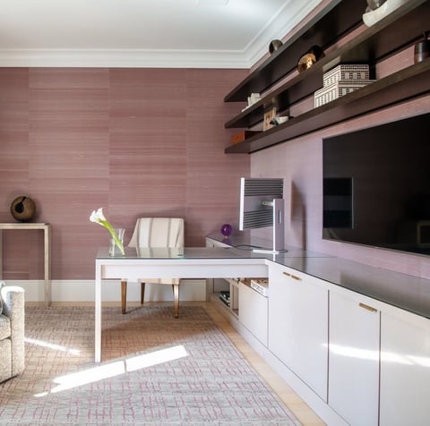 Modern home office with mauve brick walls, white desk, wall-mounted TV, floating shelves, and contemporary furnishings